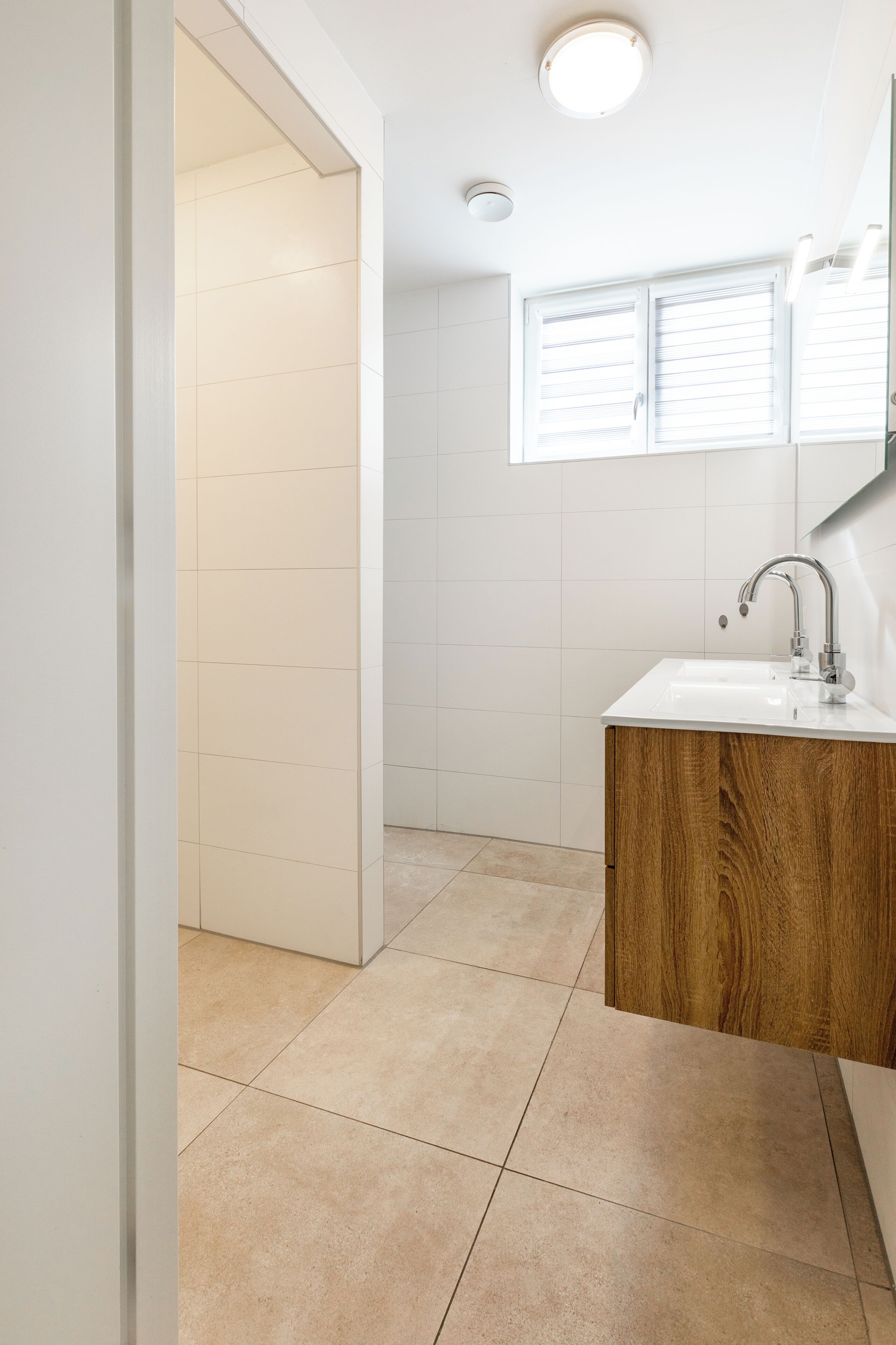 A bathroom with a white sink, wooden cabinet, and a window with blinds.