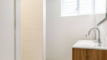 A bathroom with a white sink, wooden cabinet, and a window with blinds.