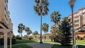 A pathway leading to a building with a covered walkway, palm trees, and a clear blue sky. - LAS ARENAS 235 - Two Bedroom Apartment, Sleeps 5 (Punta del moral)
