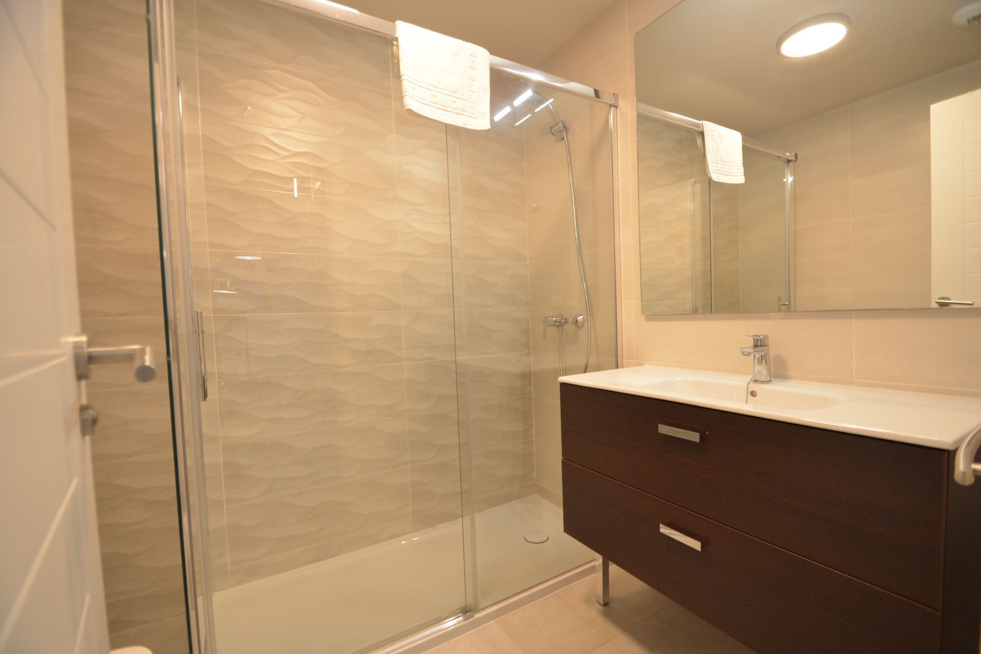Un baño moderno con ducha envuelta en vidrio, tocador de madera oscura y un espejo grande sobre el lavabo.