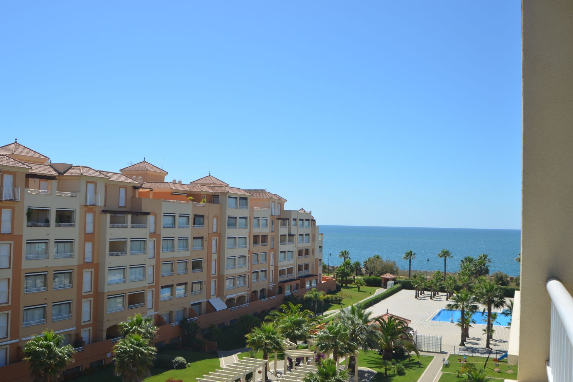 A multi-story hotel with balconies, a swimming pool, and a view of the sea.