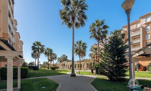 A pathway leading to a building with a covered walkway, palm trees, and a clear blue sky. - LAS ARENAS 235 - Two Bedroom Apartment, Sleeps 5 (Punta del moral)