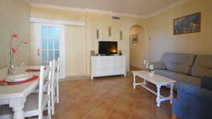Una sala de estar con un sofá gris, un mueble blanco para entretenimiento y un comedor con mesa y sillas.