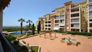 Un hotel de varios pisos con balcones, piscina y un patio ajardinado con una fuente.