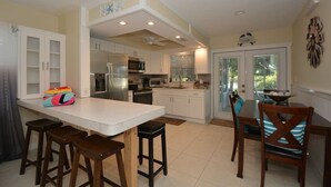 Une cuisine avec des meubles blancs, un îlot central, des tabourets de bar et une table à manger avec des chaises.