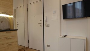 A room with a wooden floor, a white wardrobe, a white cabinet, a flat-screen TV mounted on the wall, and a small table. - Giudei House Minisuite (Bologna)