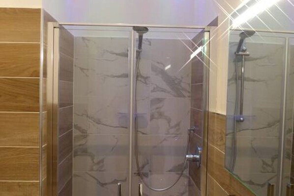 Une cabine de douche fermée par des parois en verre, avec un mur recouvert de carreaux de marbre et un panneau en bois sur un des côtés.