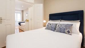 A bedroom with a large bed, white walls, and a wooden floor.