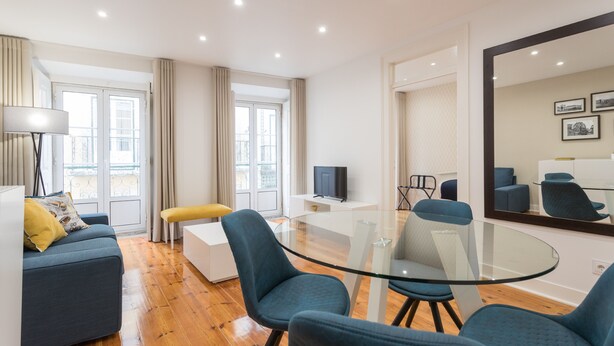 A modern living room with a glass coffee table, blue chairs, a sofa, and a television.