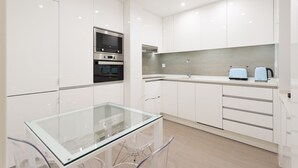 A modern kitchen with white cabinetry, a glass-top table, and stainless steel appliances.