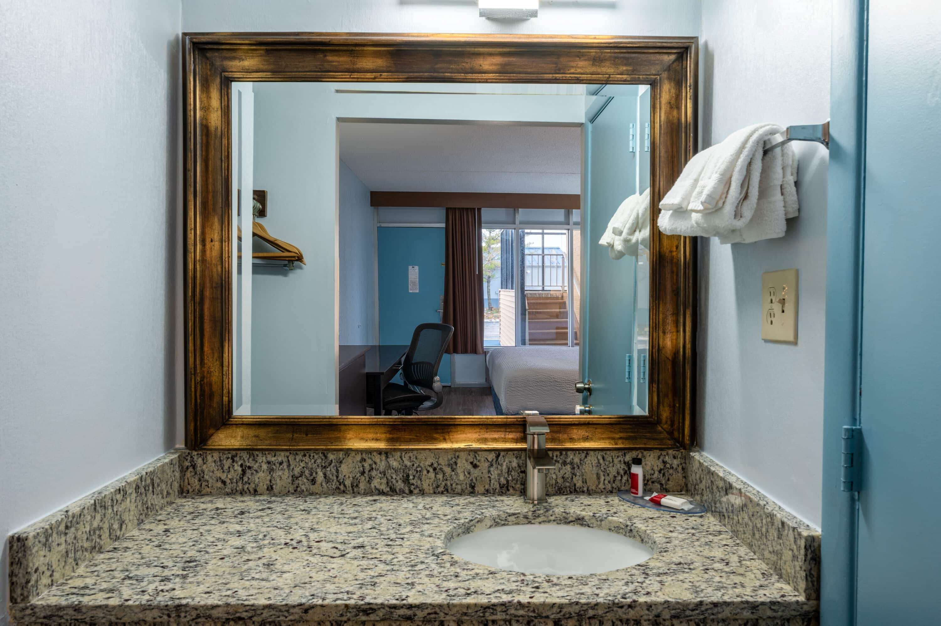 Bagno con top in granito, lavabo, specchio con cornice in legno e porta asciugamani.