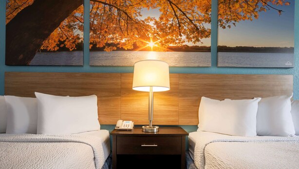 Een hotelkamer met twee bedden, een nachtkastje met een lamp, een telefoon en een schilderij van een zonsondergang boven het water.