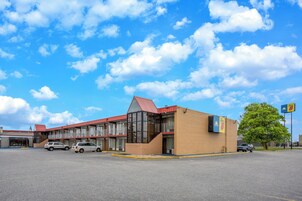 Um motel com telhado vermelho, vários andares e estacionamento.