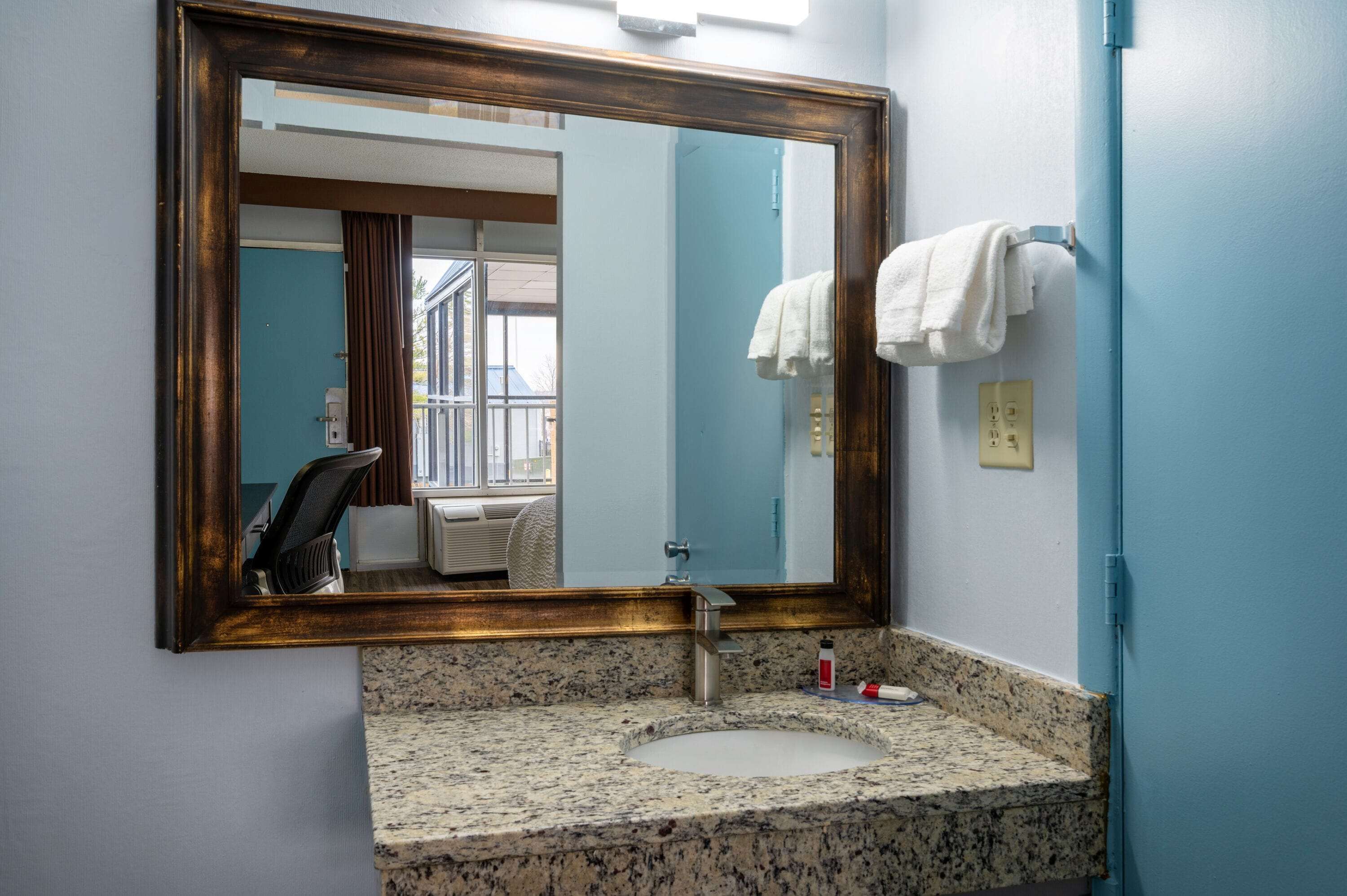 Un baño con encimera de granito, lavamanos, espejo y toallero.