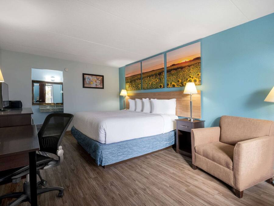 A hotel room with a bed, a desk, a chair, and a painting on the wall.
