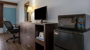 Een hotelkamer met een bureau, stoel, televisie, magnetron en koelkast.
