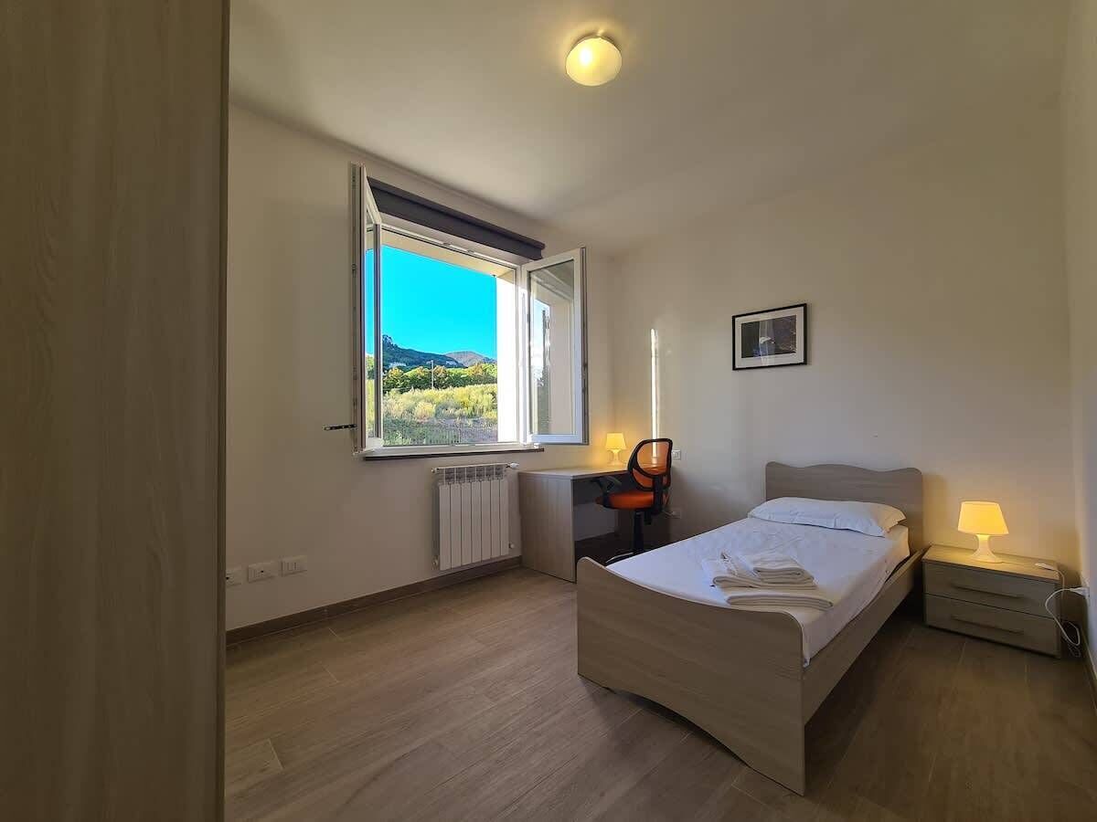 Ein Schlafzimmer mit Bett, Schreibtisch, Stuhl, Heizkörper, einem Fenster mit Blick und einem Wandbild.