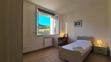 Ein Schlafzimmer mit Bett, Schreibtisch, Stuhl, Heizkörper, einem Fenster mit Blick und einem Wandbild.