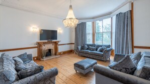 A living room with a fireplace, two sofas, a television, and a chandelier. - A luxurious Victorian mansion garden apartment (Broughty Ferry)