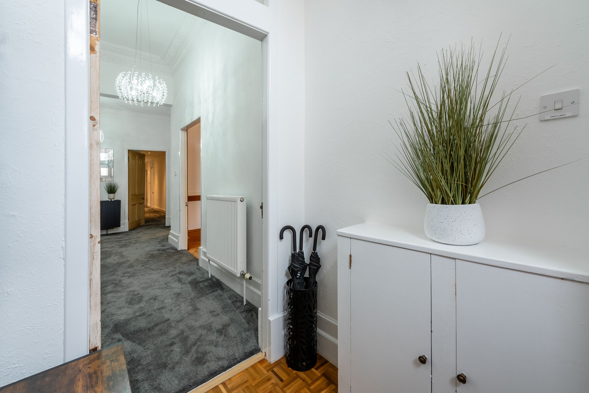 A hallway with a radiator, a potted plant, and a black umbrella leaning against the wall.
