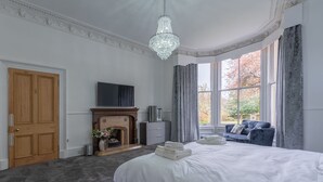 A bedroom with a large bed, a fireplace, a TV, and a window with curtains. - A luxurious Victorian mansion garden apartment (Broughty Ferry)