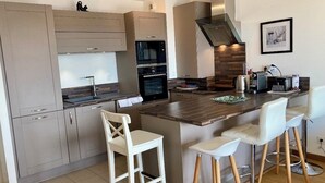 A modern kitchen with grey cabinets, a central island with stools, a built-in oven, and a stainless steel range hood. - Appt terrasse vue mer, 2 chambres / Appt terrace sea view with 2 bedrooms (Trouville-sur-Mer)