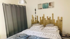 Ein Schlafzimmer mit Bett, grauen Vorhängen, einem hölzernen Kopfende und einem Wandbild.
