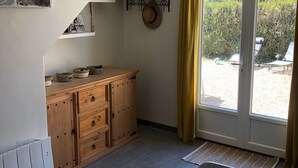 Ein Zimmer mit einem Holzkasten, einem hängenden Korb mit dem Aufdruck „Französische Riviera“, einem Hut auf einem Wandhaken und Blick auf einen Außenbereich durch eine Tür.
