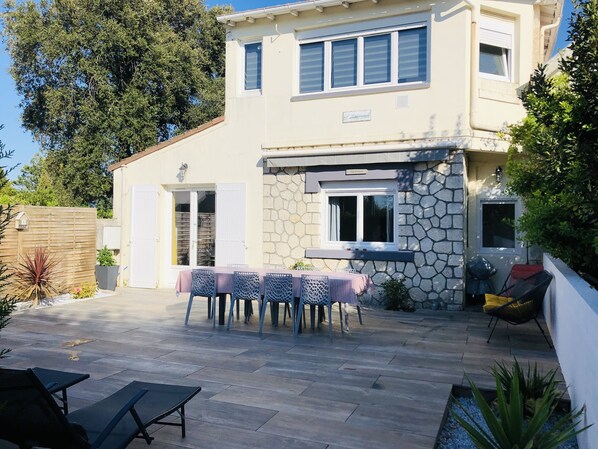 A two-story house with a stone facade, a patio with a table and chairs, and a small garden area.