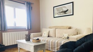 Ein gemütliches Wohnzimmer mit einem gestreiften Sofa, einem weißen Couchtisch, einem Korbstuhl und einem gerahmten Bild an der Wand.