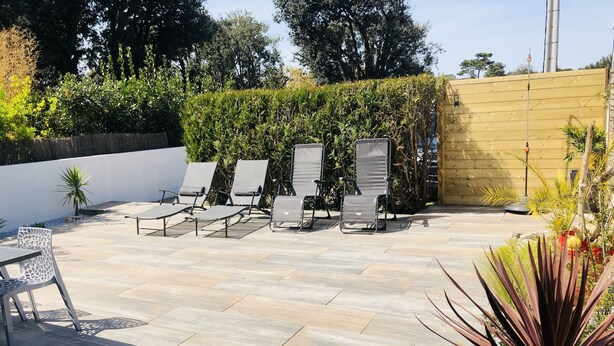 Eine Terrasse mit Liegestühlen und einem Tisch, umgeben von einem Holzzaun und viel Grün.