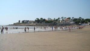 Ein belebter Strand mit badenden Menschen, einem sandigen Ufer und Gebäuden im Hintergrund.