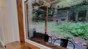 Una mesa de madera con un plato de comida y una taza, junto a una ventana con vistas a un jardín.