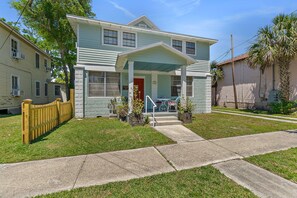A two-story house with a front porch, a red door, and a small front yard.