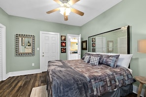 A bedroom with a bed, a ceiling fan, a large mirror, and a door leading to a bathroom.