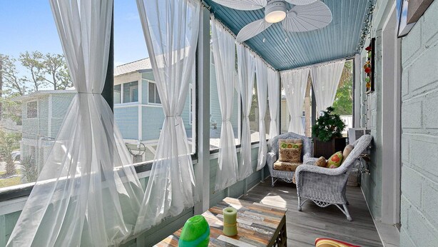 Eine überdachte Veranda mit Deckenventilator, Korbmöbeln und Blick ins Freie.