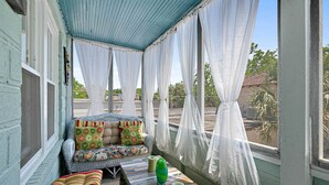 Eine überdachte Veranda mit gepolsterten Sitzgelegenheiten, einem Tisch mit einer Vase und transparenten Vorhängen.