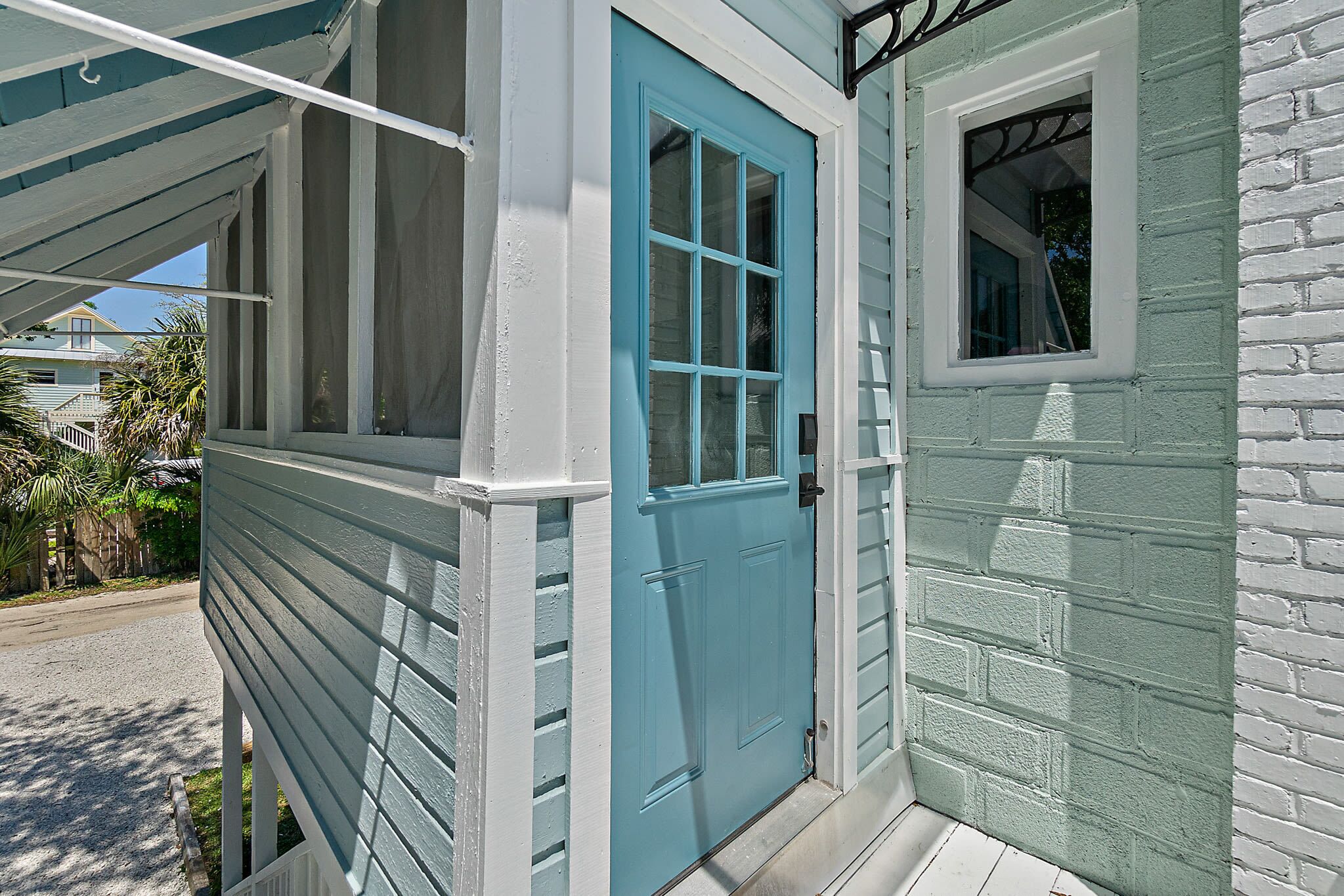Une maison avec une porte bleue, une petite fenêtre et une véranda dotée d’une balustrade blanche.