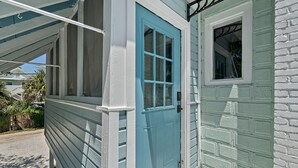 Ein Haus mit einer blauen Tür, einem kleinen Fenster und einer Veranda mit weißer Brüstung.