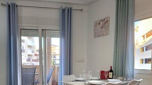 A dining area with a table set for four, a bottle of wine, and a view through a glass door to an outdoor balcony. - Frontline modern- Cabo del Playa- Apartment (Cabo Roig)
