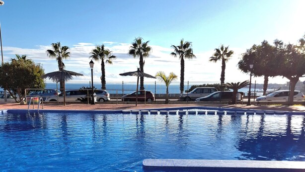 A clear blue pool with a tiled edge, surrounded by palm trees and a view of the ocean. - Frontline modern- Cabo del Playa- Apartment (Cabo Roig)
