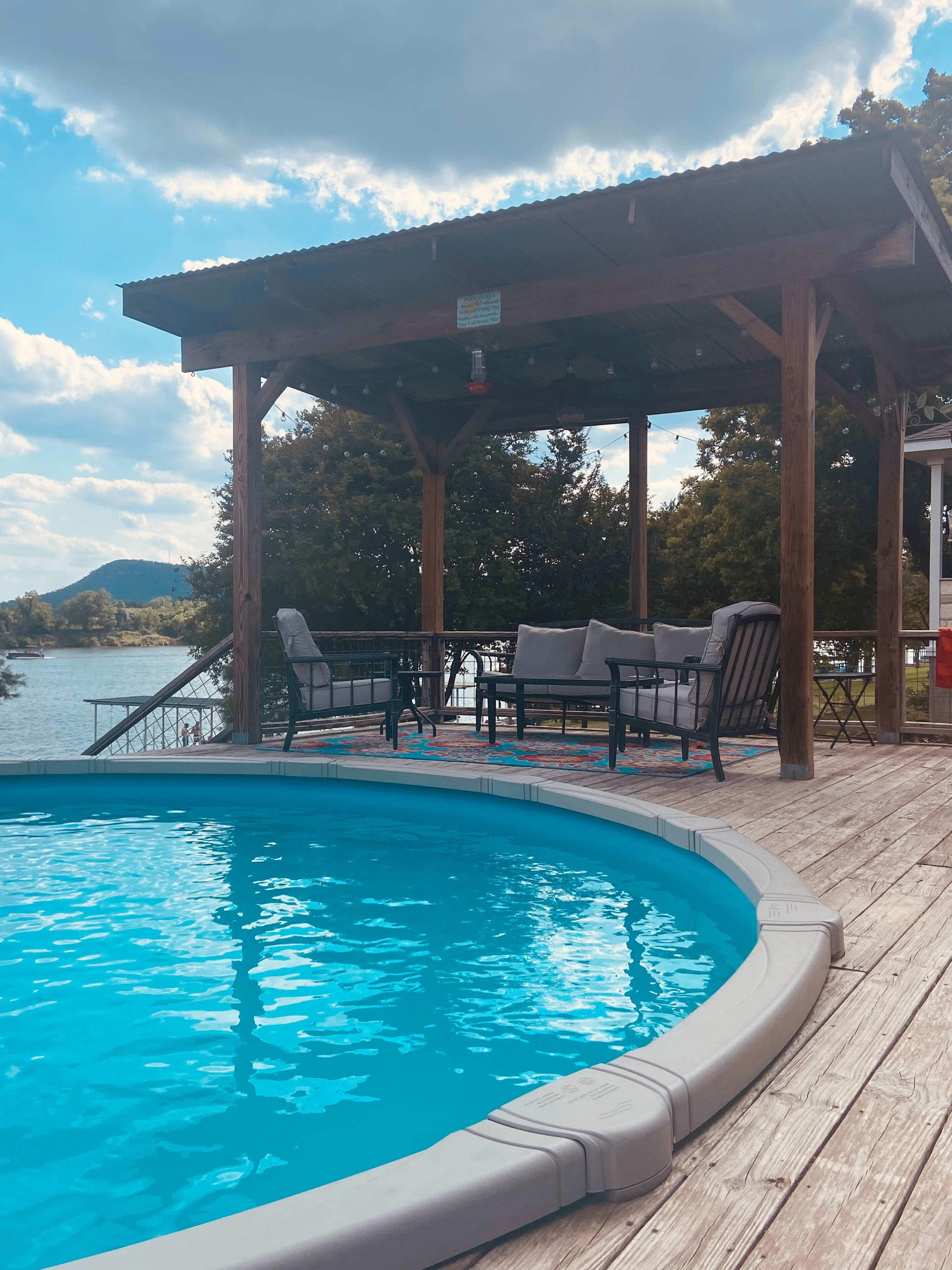 A wooden deck with a pool, outdoor furniture, and a pergola.