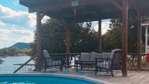 Eine Holzterrasse mit Pool, Gartenmöbeln und einer Pergola.