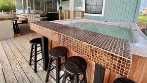 Ein Whirlpool mit gefliestem Rand, einer Holzdielen-Terrasse und zwei Hockstühlen.
