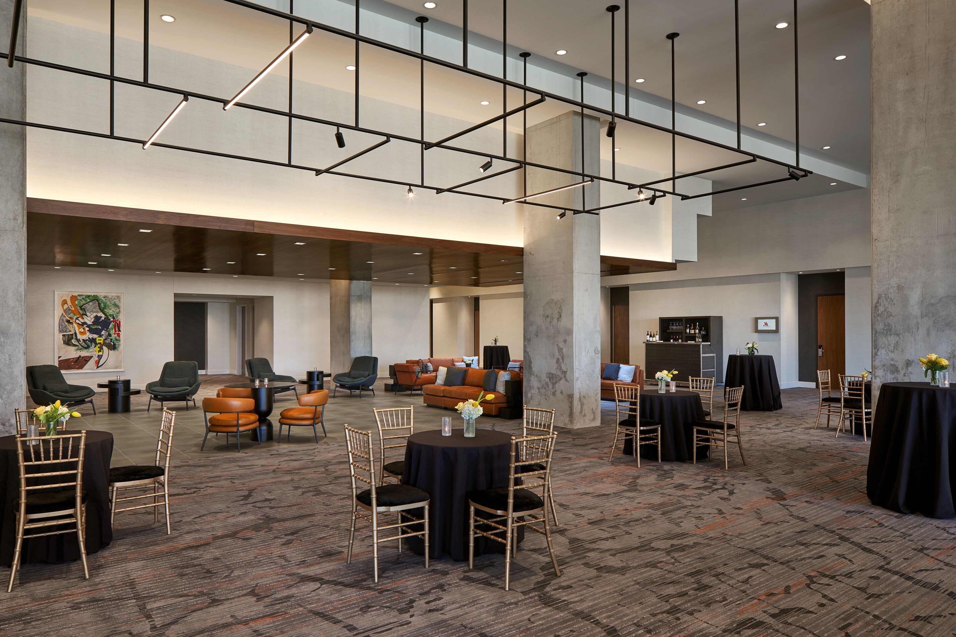 A spacious hotel lobby with high ceilings, modern lighting, and multiple seating areas including round tables and chairs.