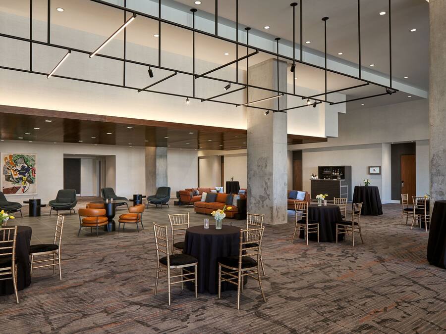 A spacious hotel lobby with high ceilings, modern lighting, and multiple seating areas including round tables and chairs.
