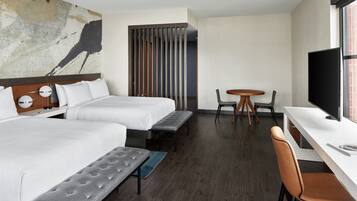 Habitación de hotel con dos camas, un escritorio, una silla, un televisor y un cuadro abstracto grande en la pared.