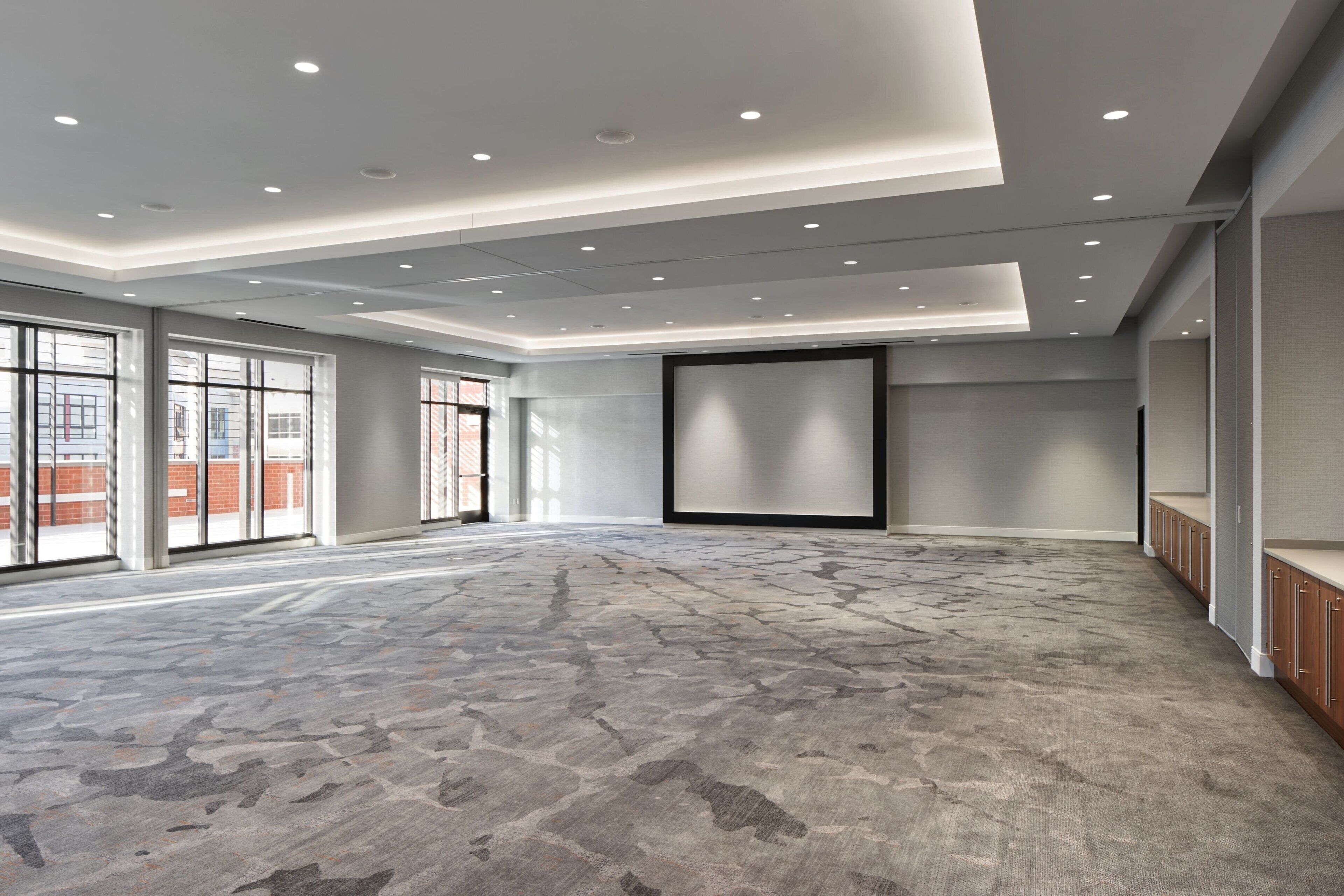 A spacious, well-lit conference room with a patterned carpet, large windows, and a modern ceiling design.