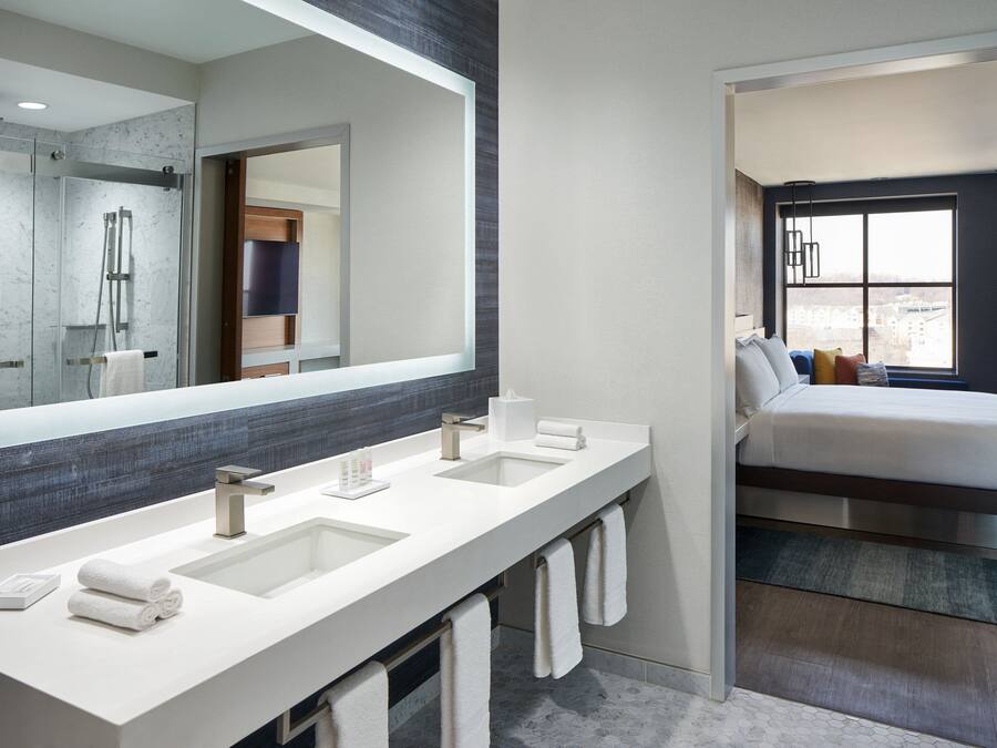 A modern bathroom with a large mirror, two sinks, and a shower.