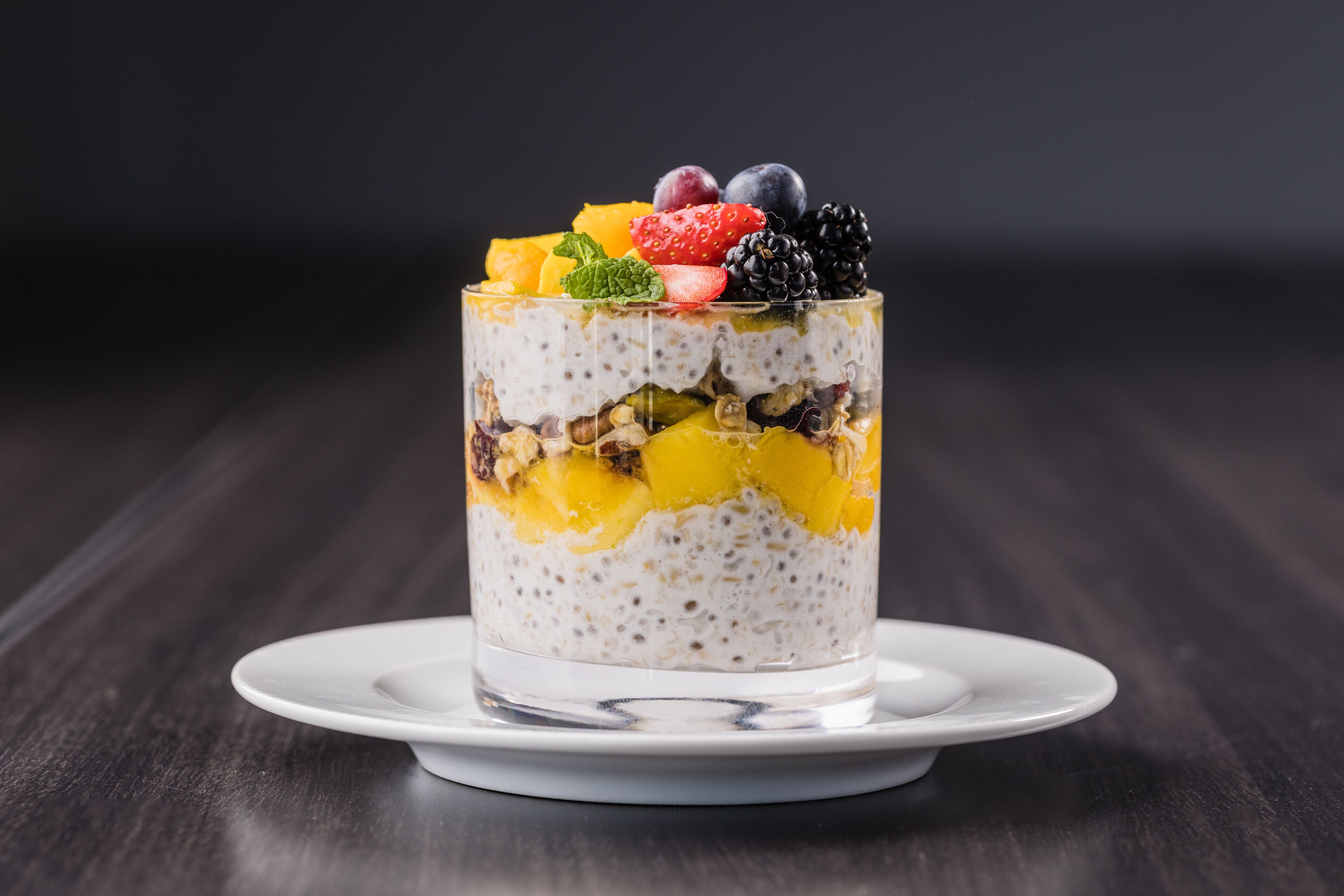 Un dessert stratificato in un bicchiere trasparente su un piatto bianco.
